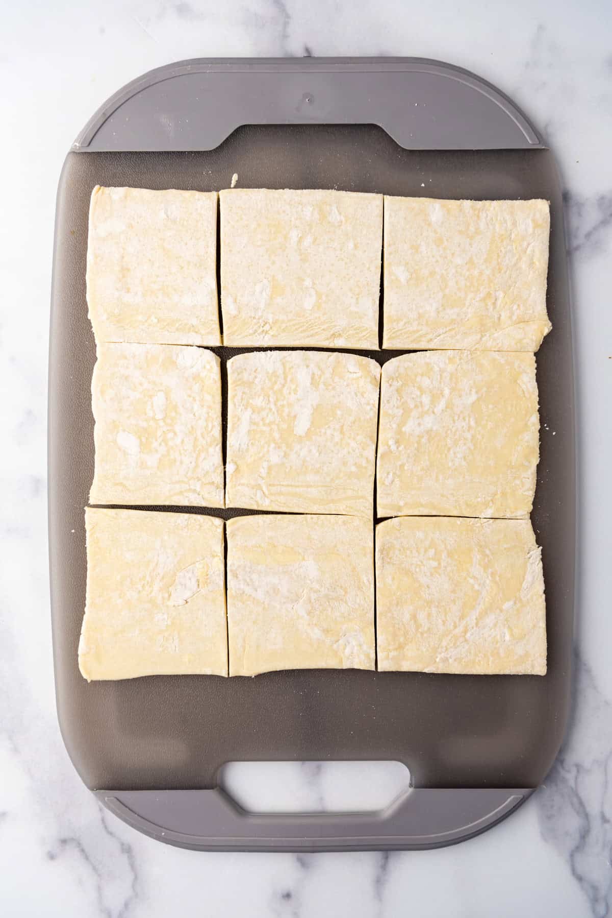 Puff pastry cut into squares on a cutting board.