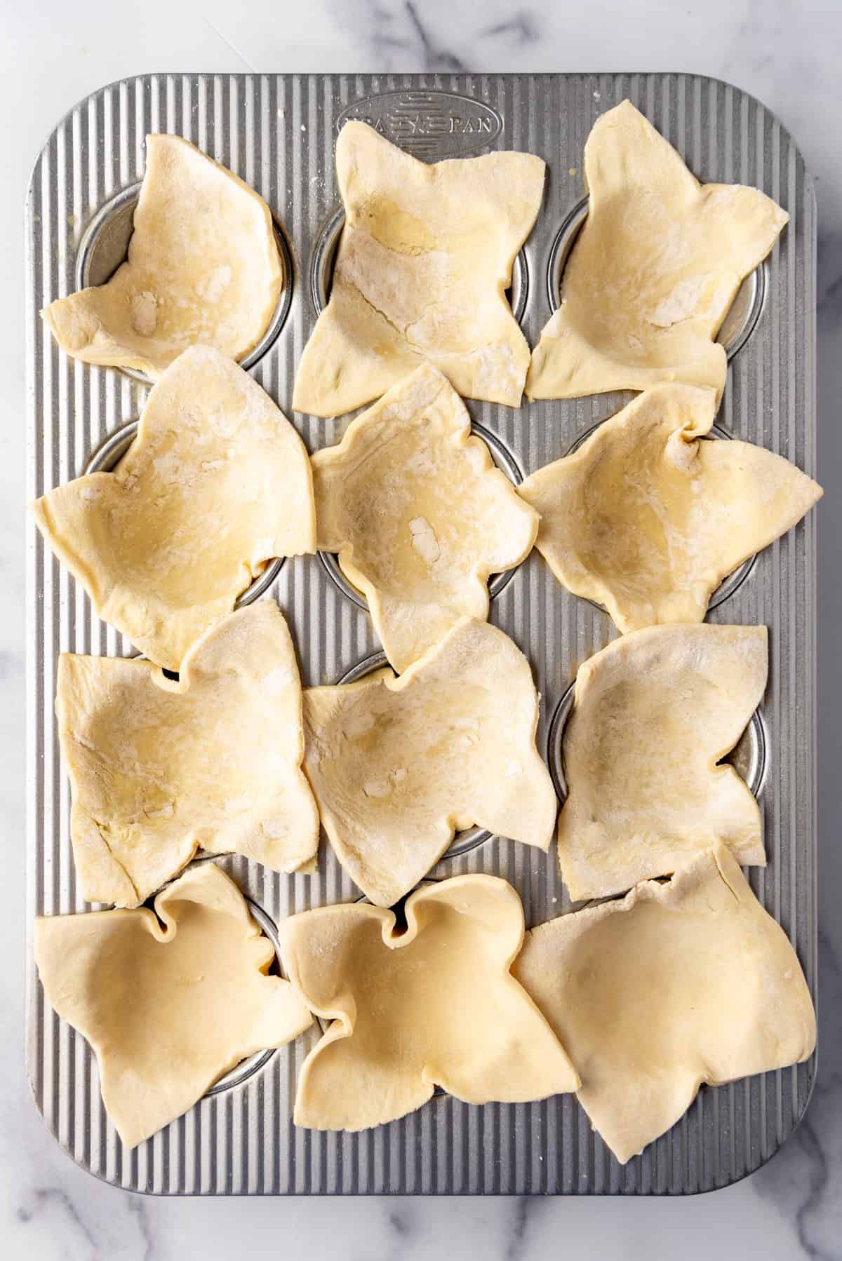 An image of puff pastry cut into squares and placed in a muffin pan.