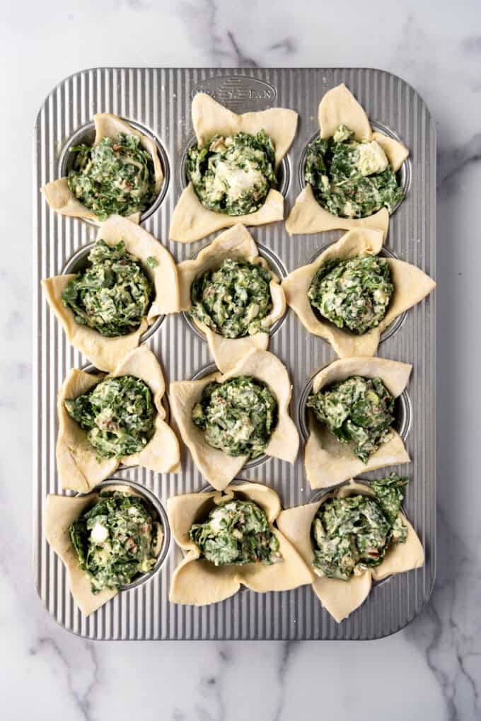 Adding spinach filling to puff pastry in a muffin pan.