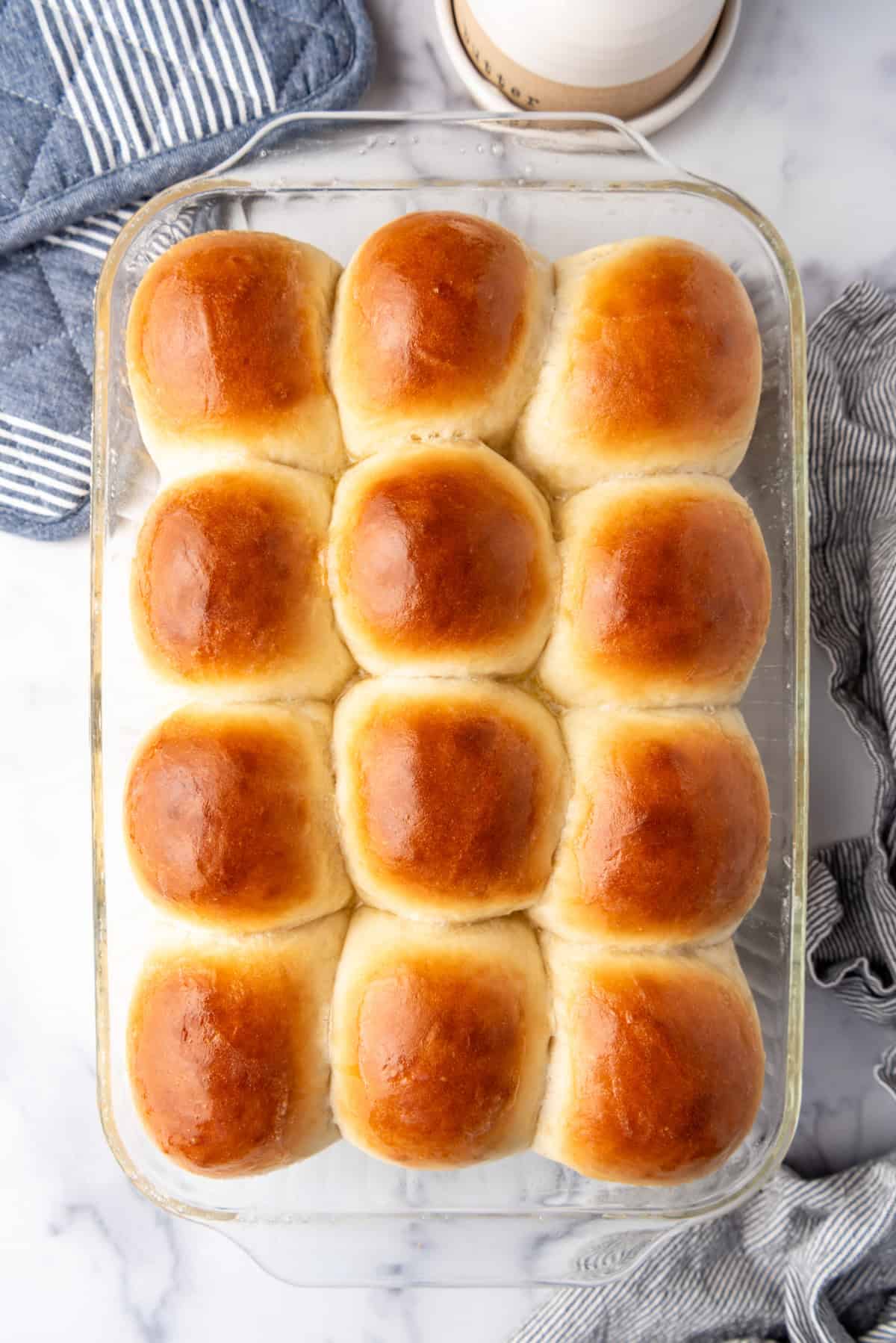 A dozen baked dinner rolls in a glass baking pan.