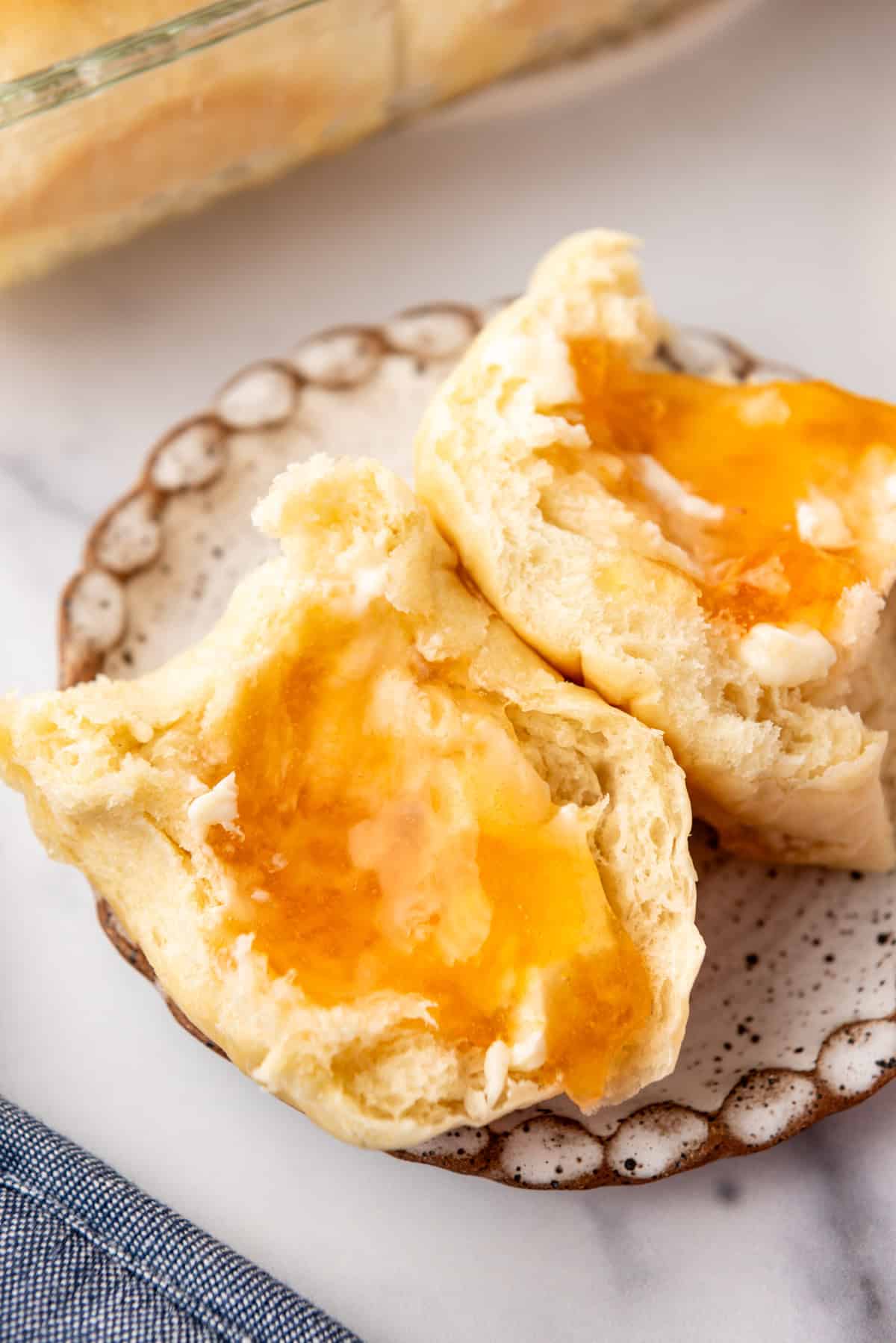 An image of a dinner roll that has been sliced open with butter and peach jam on it.