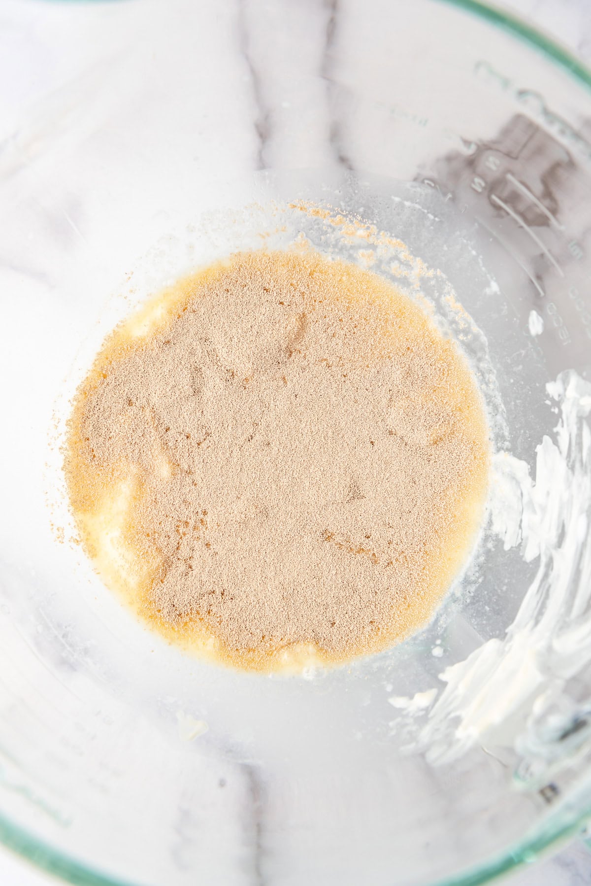 Adding yeast to warm liquid in a bowl.