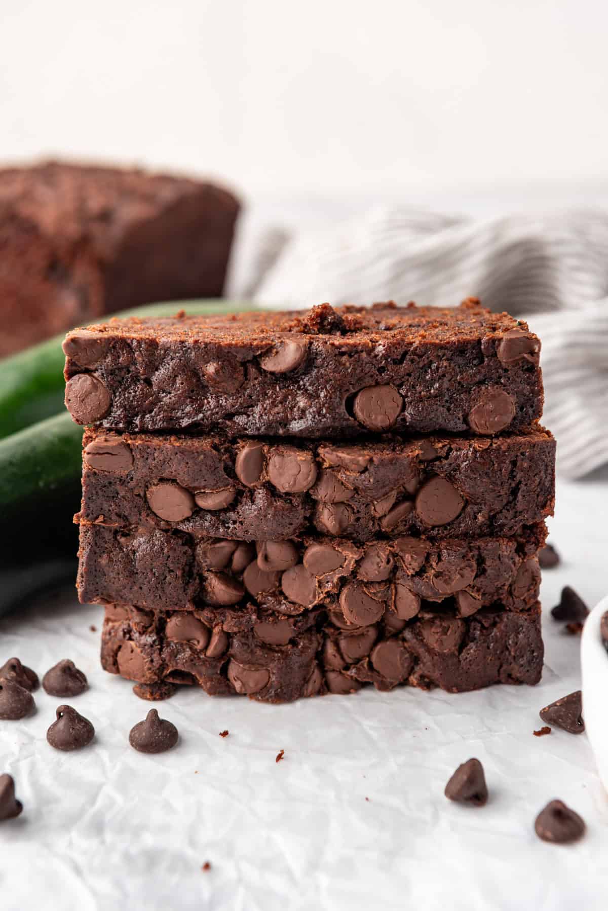 Tranches de pain au chocolat et courgette empilées sur une surface blanche avec des courgettes et des pépites de chocolat autour d'elles.