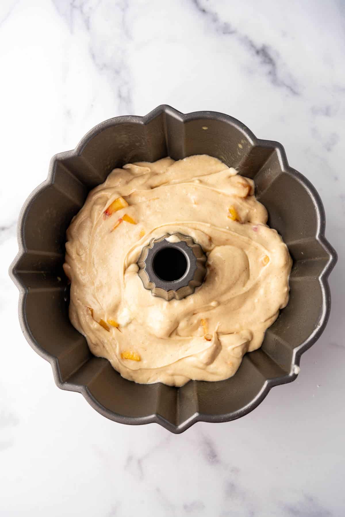 Adding peach pound cake batter to a bundt pan.