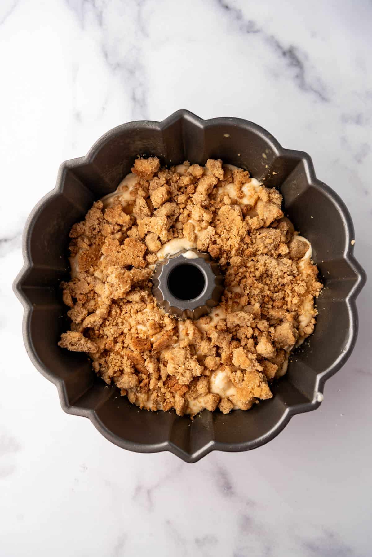 Adding crumb topping to pound cake batter in a bundt pan.