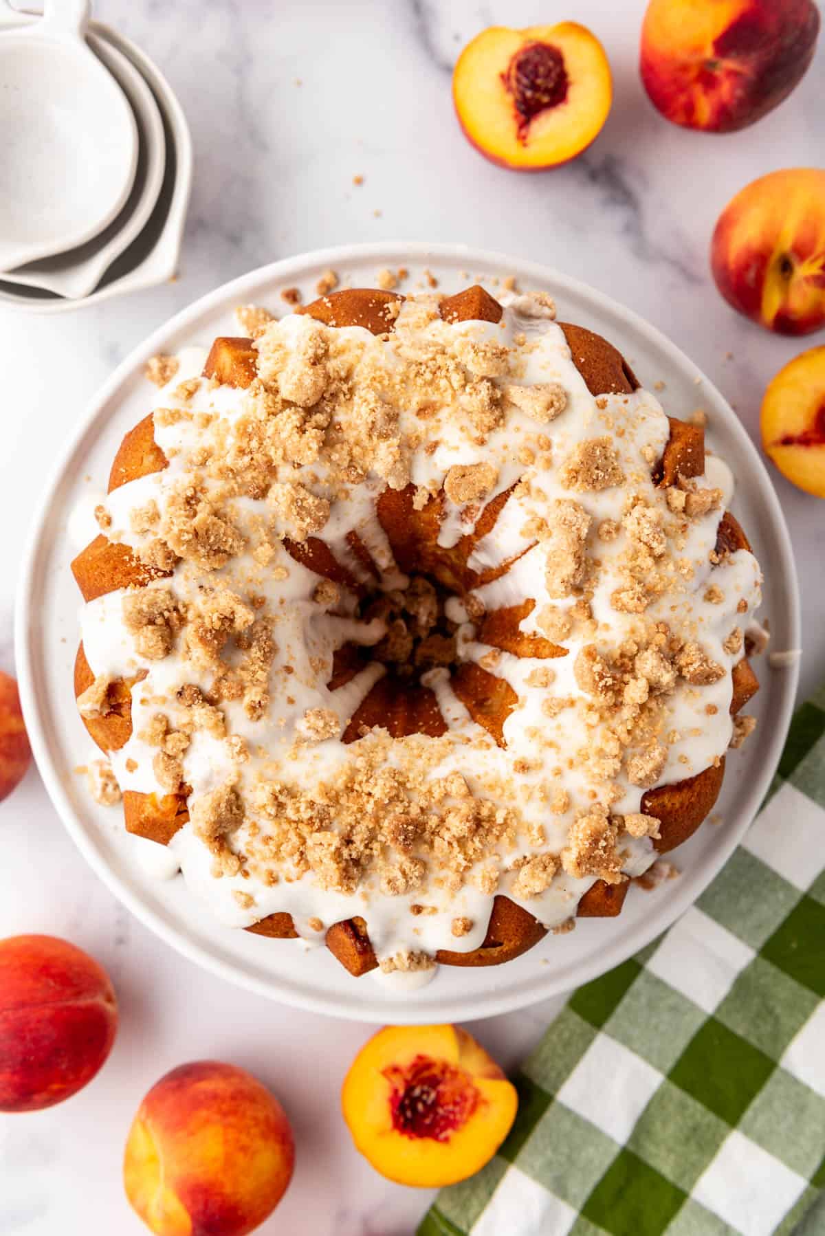 An overhead image of a peach cobbler pound cake with fresh peaches and a green and white napkin.