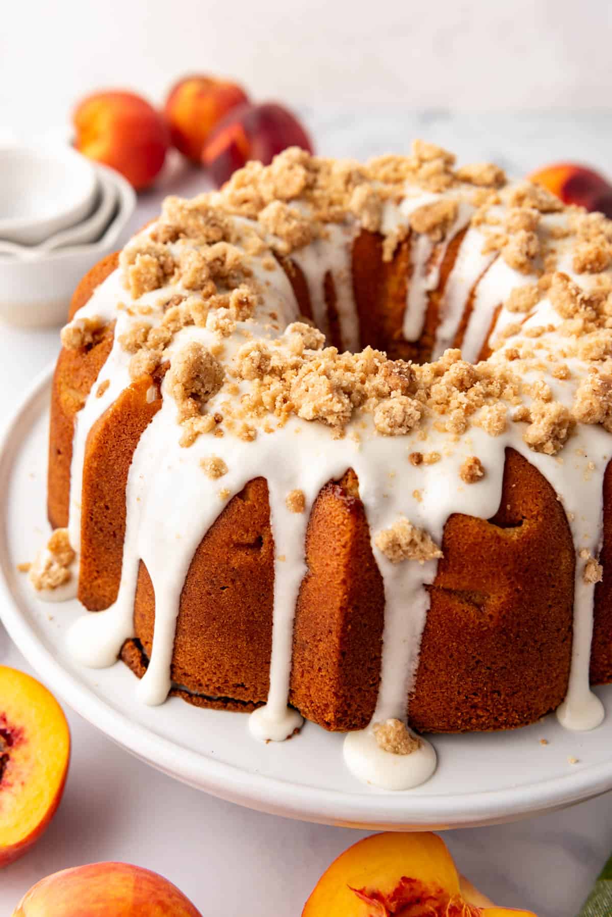 A peach cobbler pound cake with glaze and crumble topping on it.