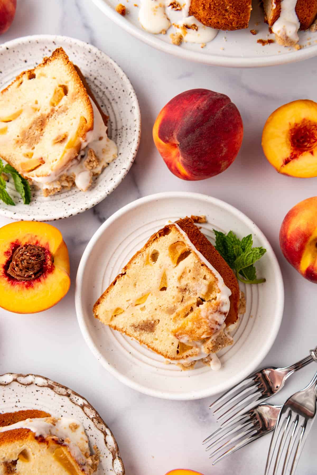 Slices of peach cobbler pound cake on white plates next to fresh peaches.