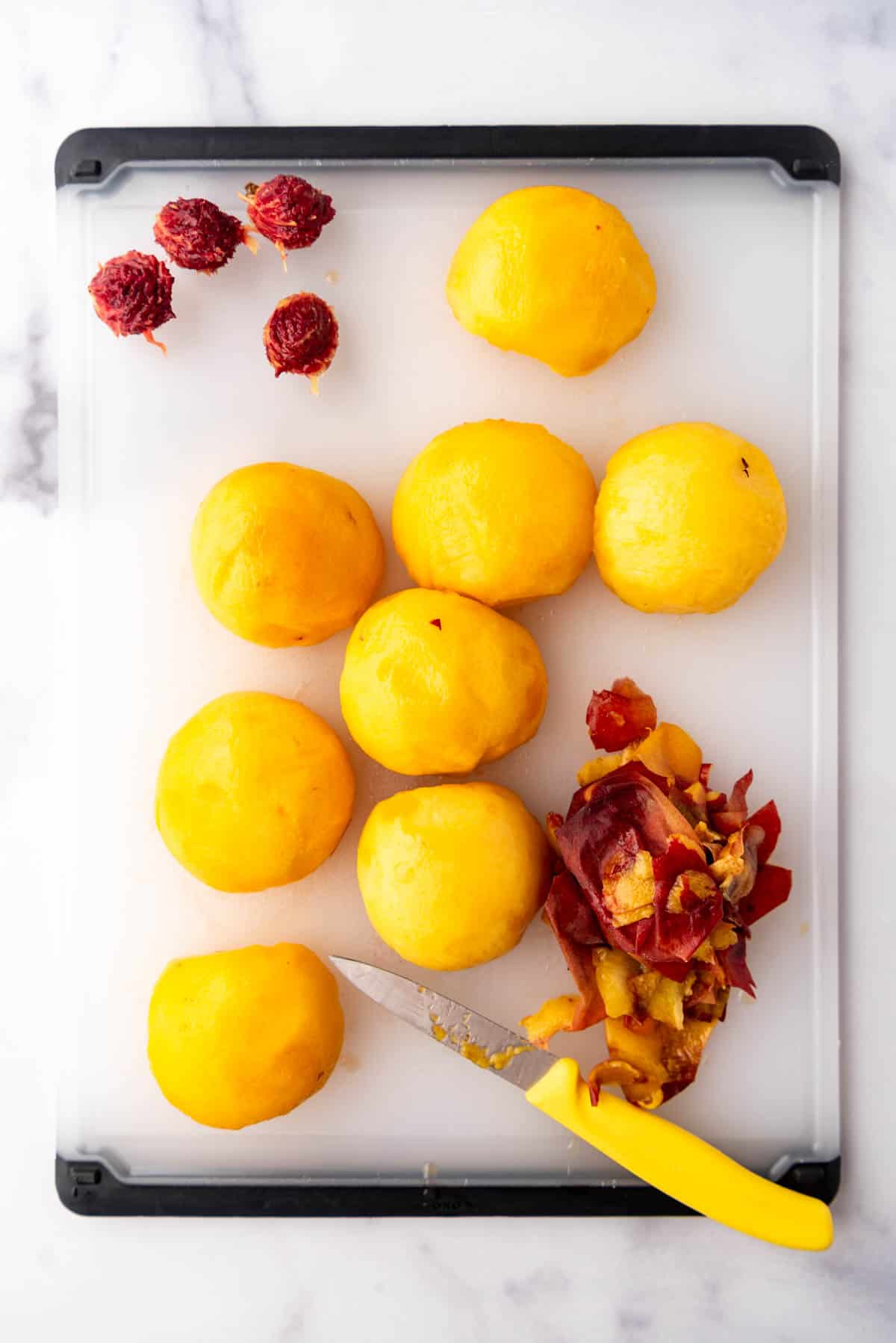 Peeled peaches on a cutting board with a paring knife.