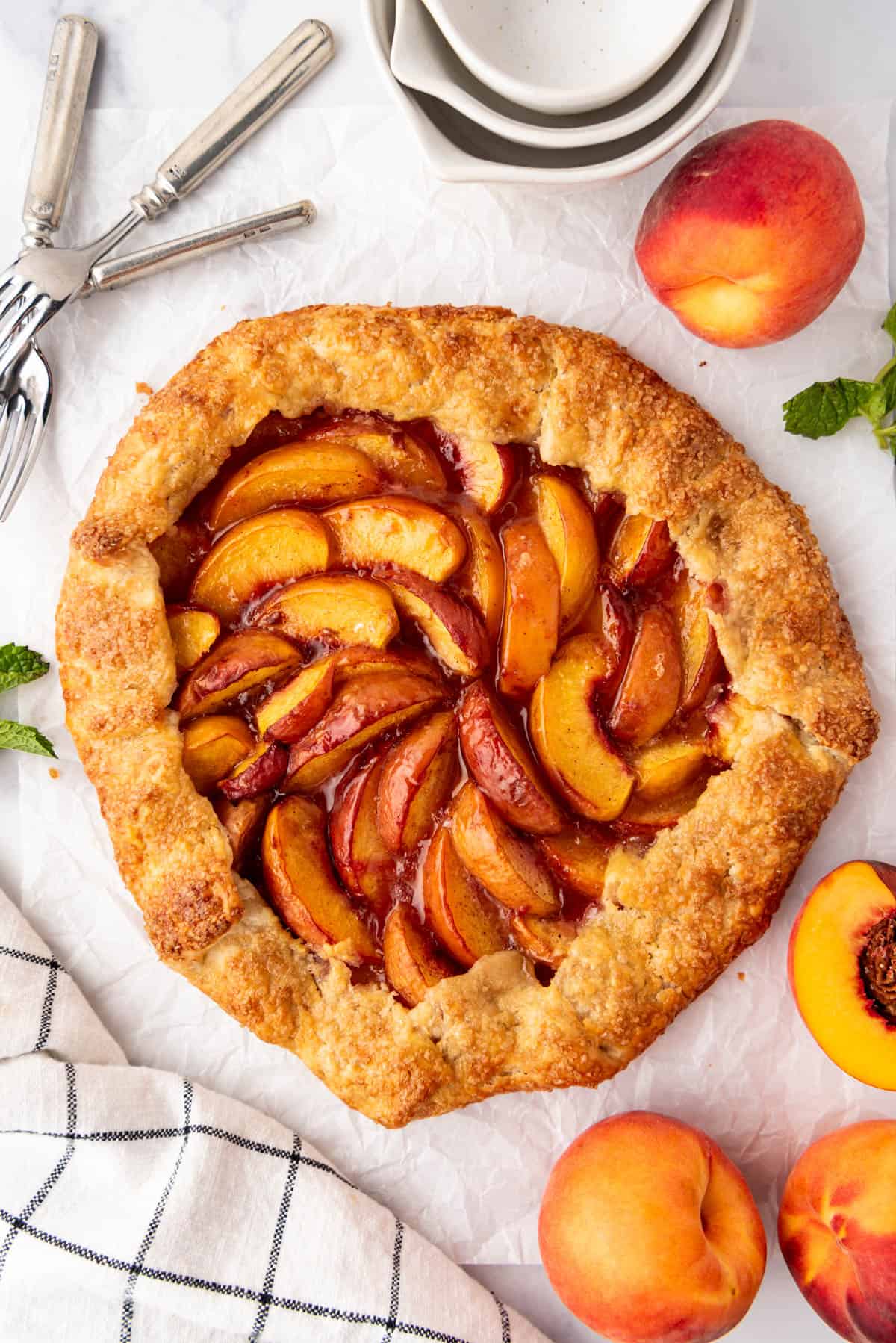 An overhead image of a peach galette with fresh peaches nearby.