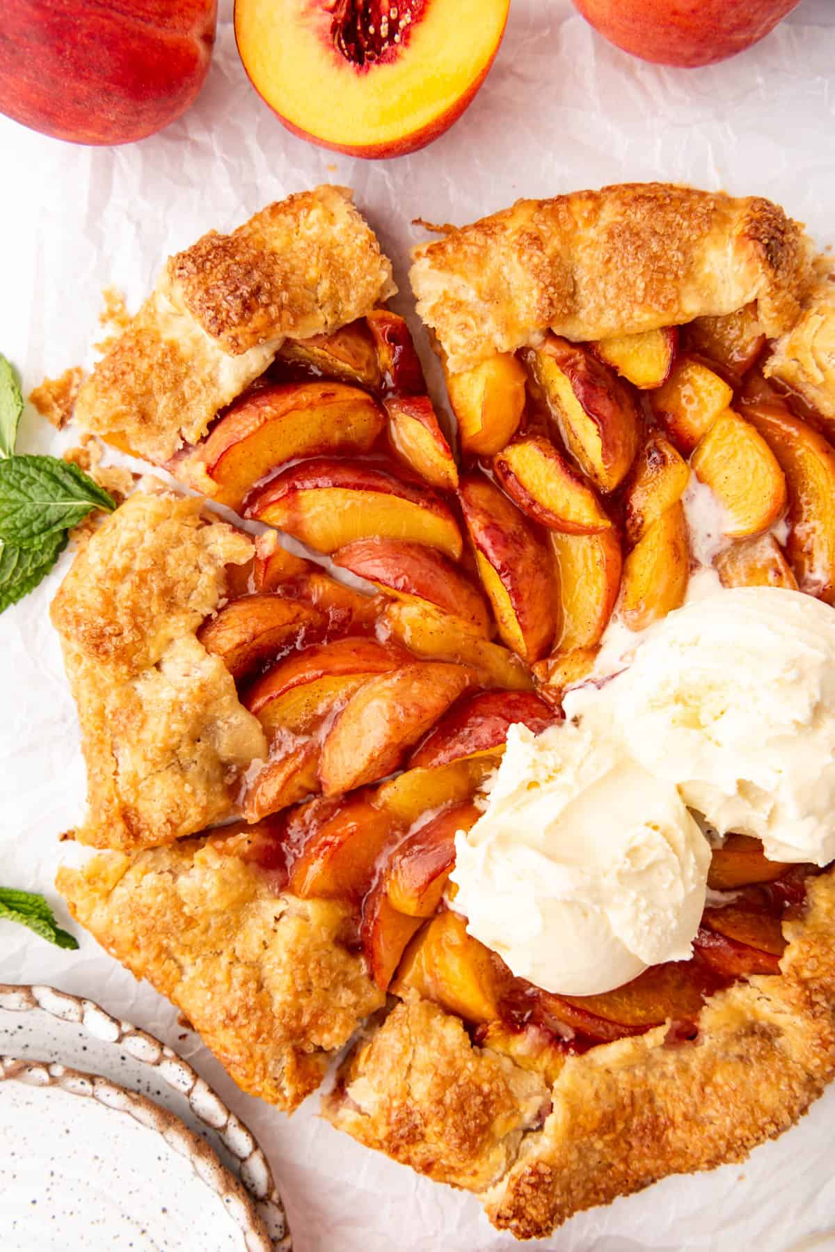 An overhead image of a sliced peach galette with scoops of vanilla ice cream on top.