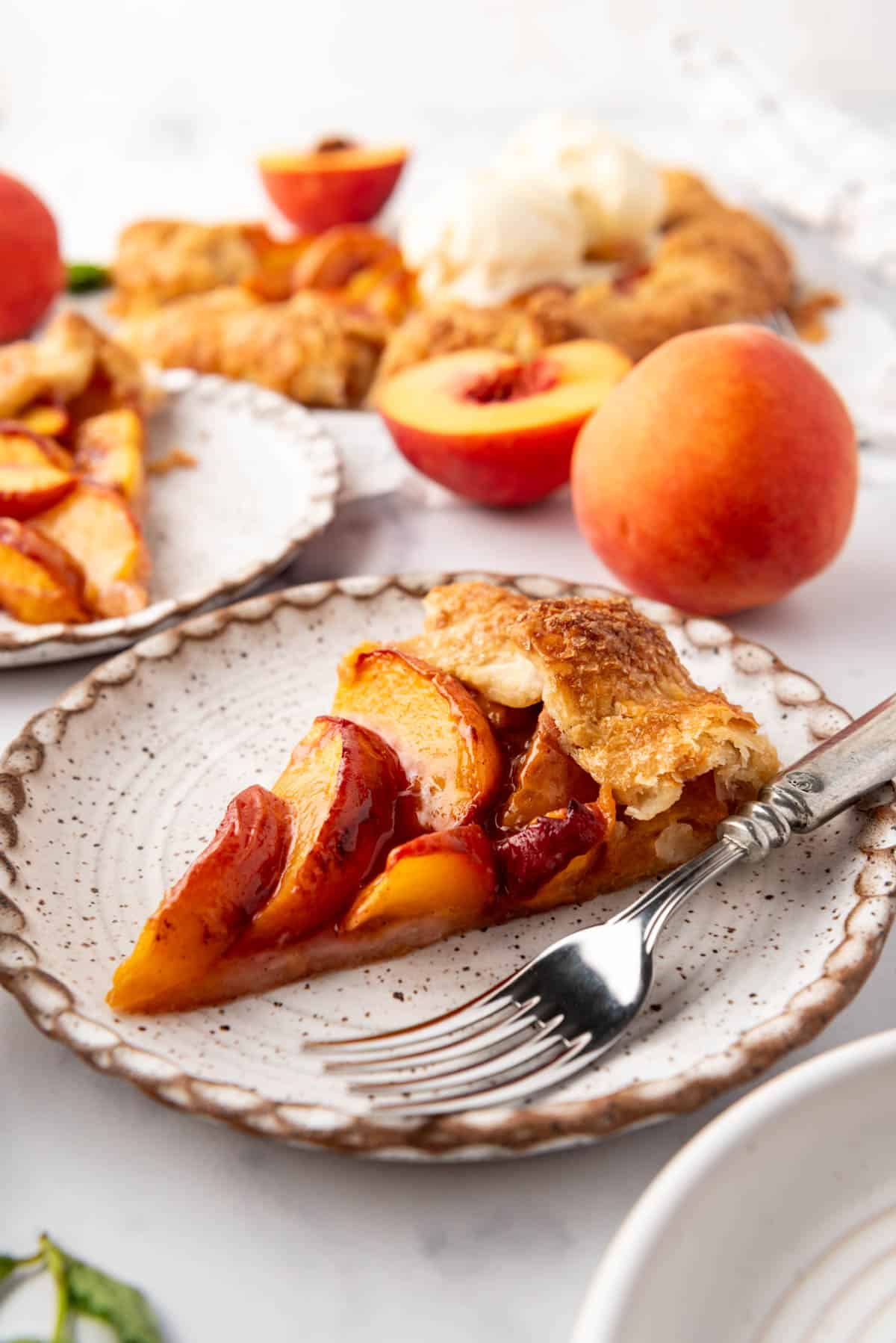 A slice of fresh peach galette on a plate with a fork.