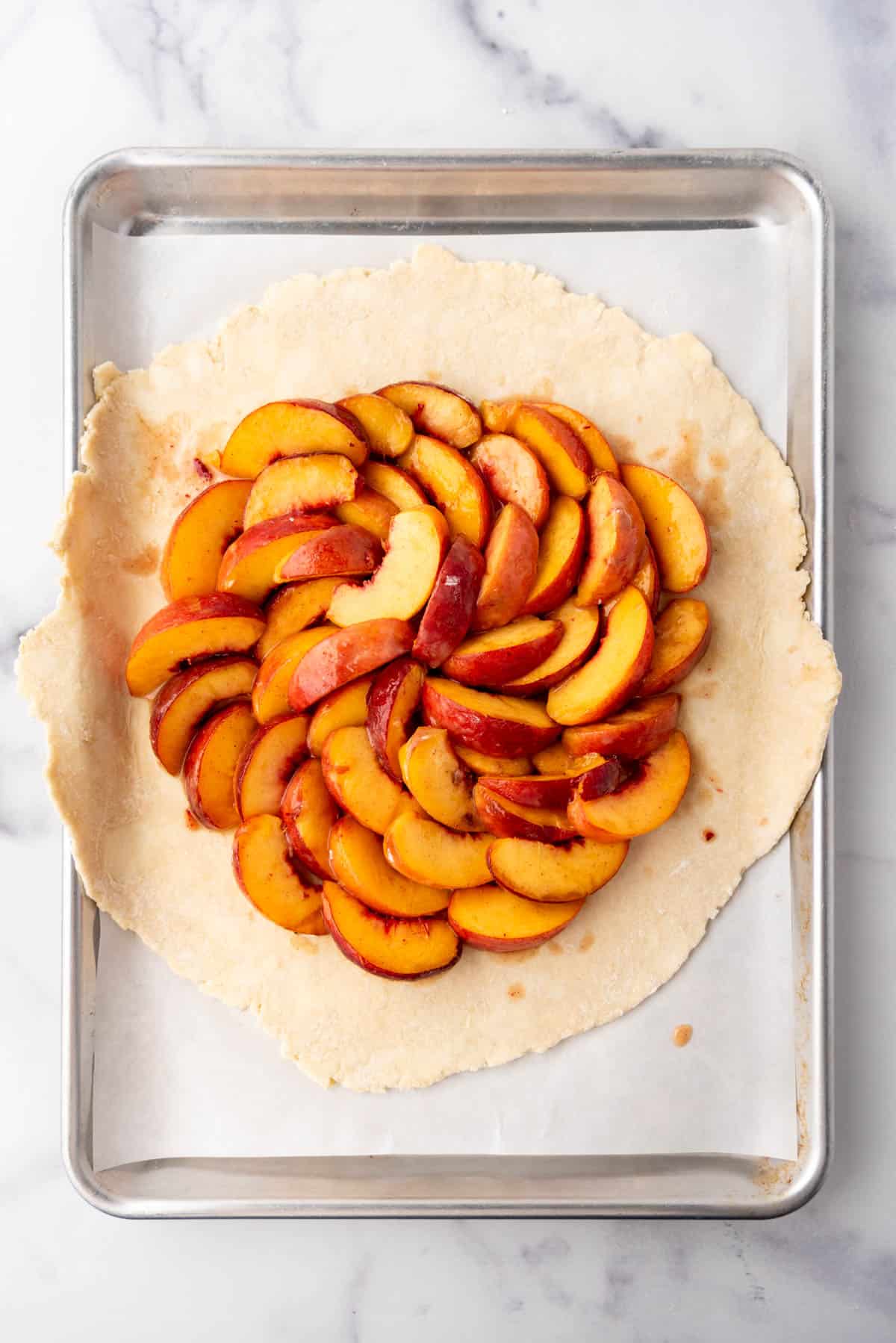 Arranging peach slices on top of a pie crust on a baking sheet to make a galette.