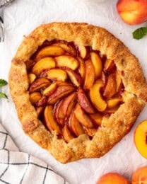 An overhead image of a peach galette with fresh peaches nearby.