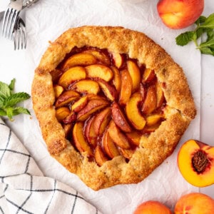 An overhead image of a peach galette with fresh peaches nearby.