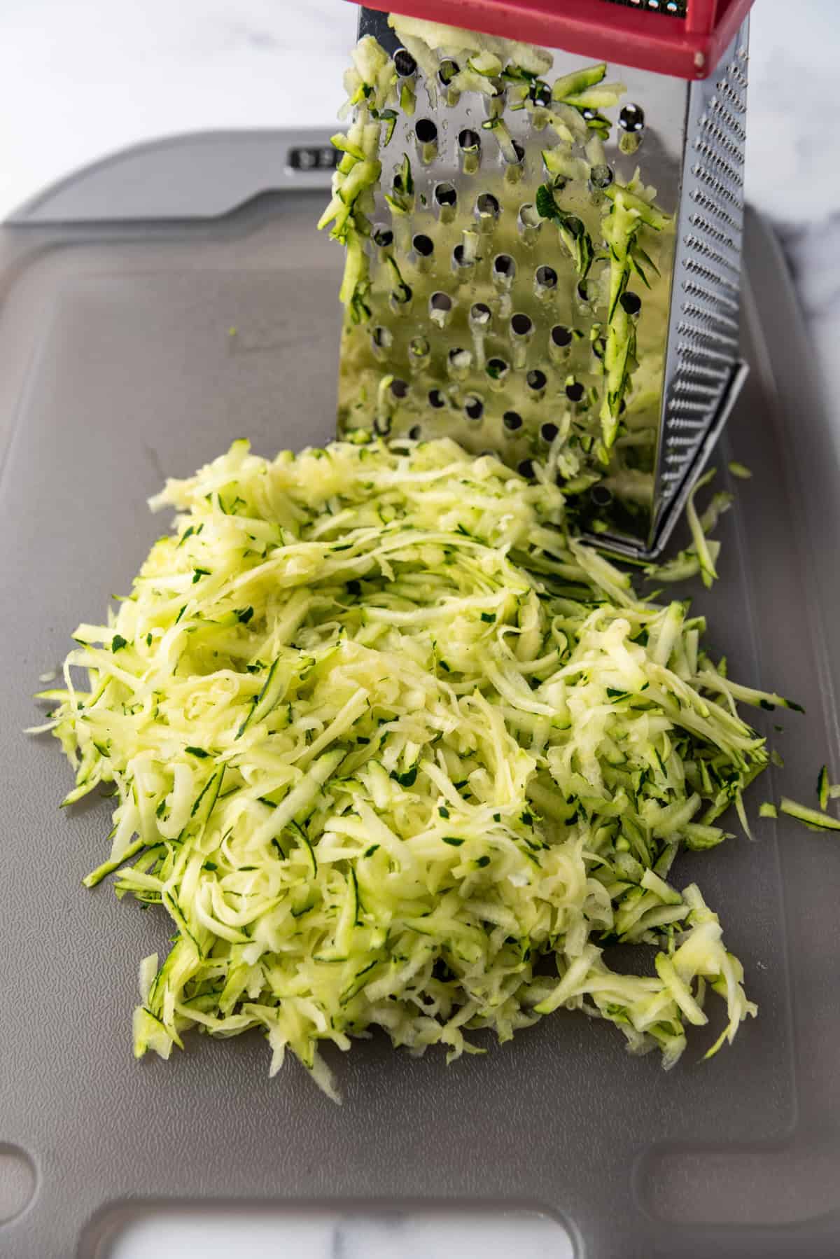 Grated zucchini next to a grater on a plastic chopping board.