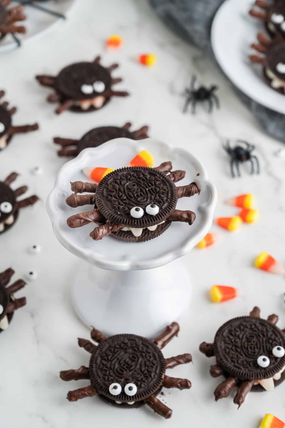 Oreo Halloween spiders with pretzel legs with one of a small white cake stand.