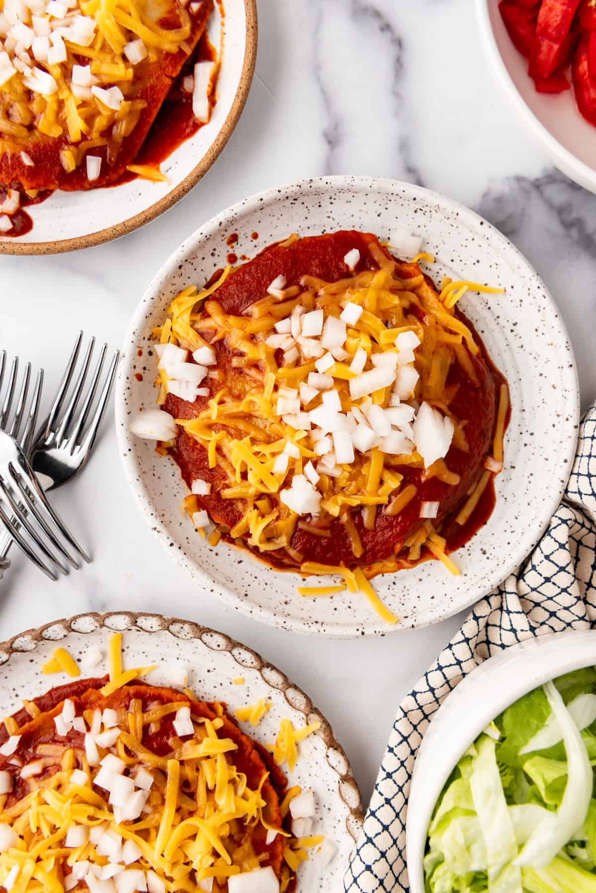 Une image vue de haut d'enchiladas au fromage empilées, garnies de fromage râpé et d'oignon blanc haché.