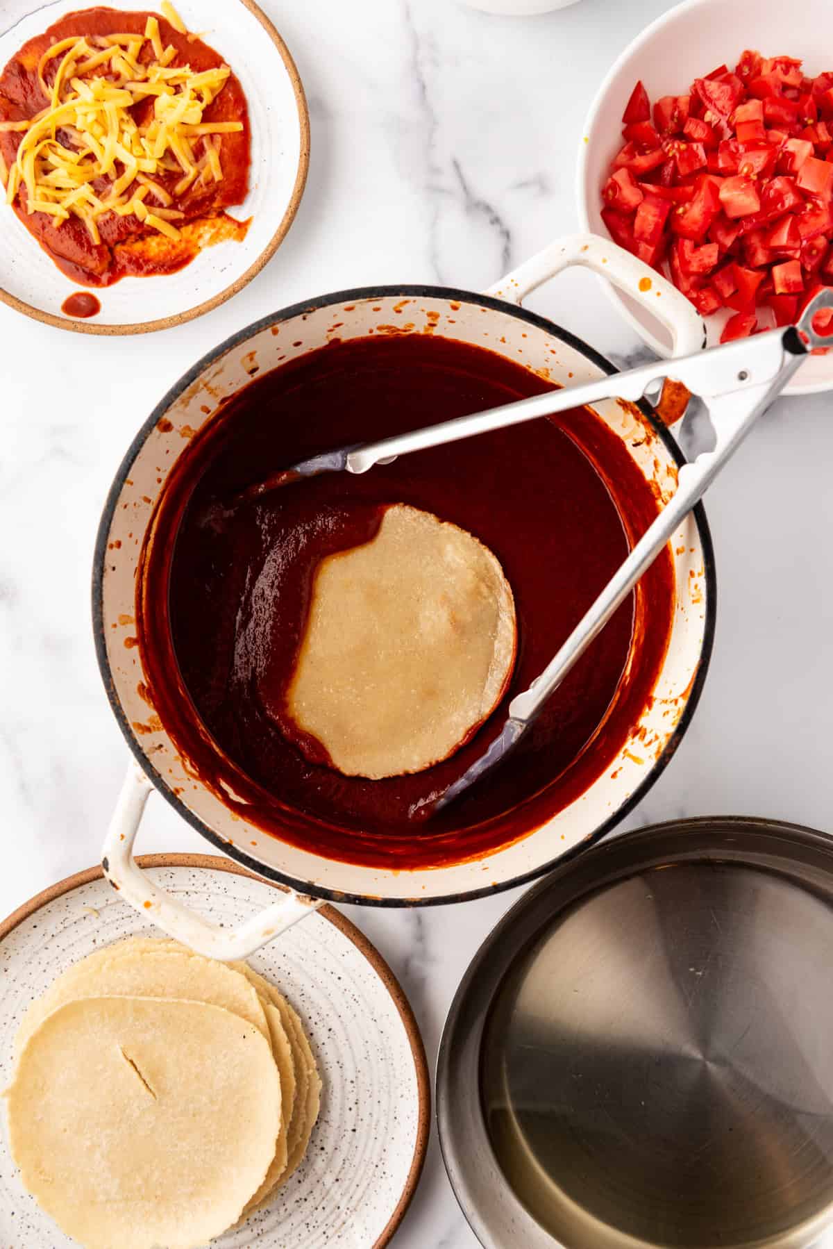 Dipping homemade corn tortillas into homemade enchilada sauce.