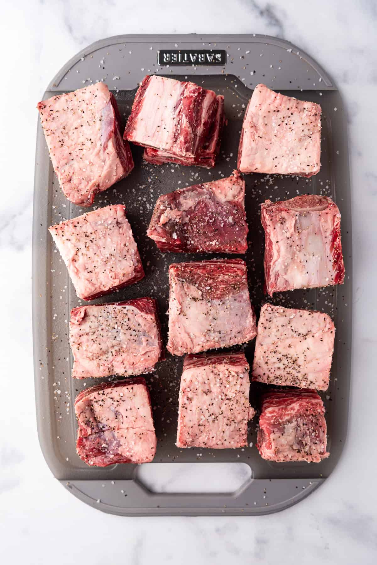 Overhead image of seasoned short ribs on a grey chopping board.