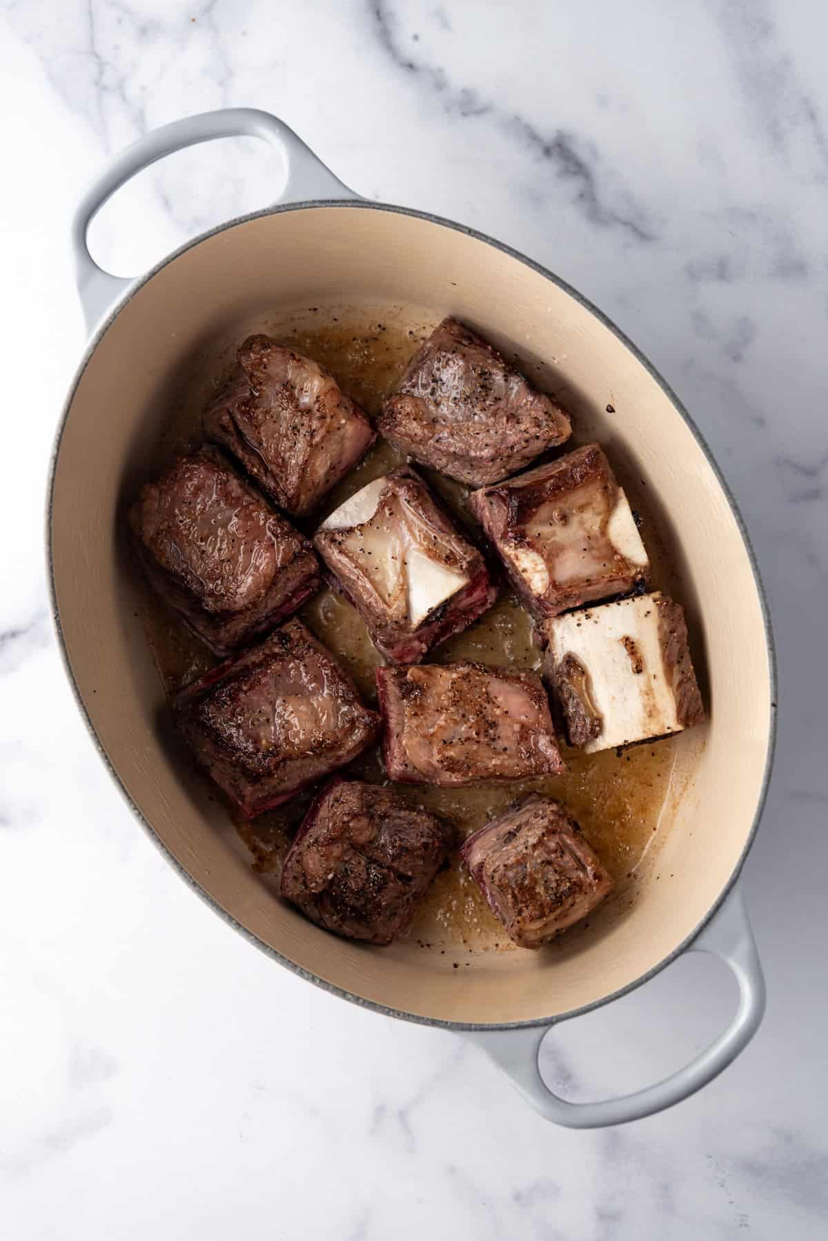 Overhead image of seared short ribs in a large dutch oven.