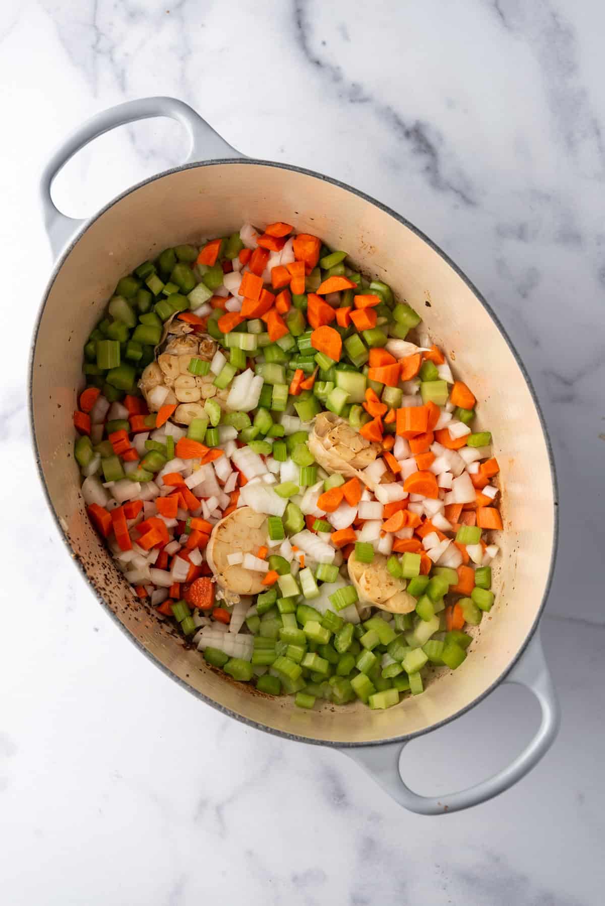 Overhead image of large dutch oven containing garlic, onion, celery, and carrots.