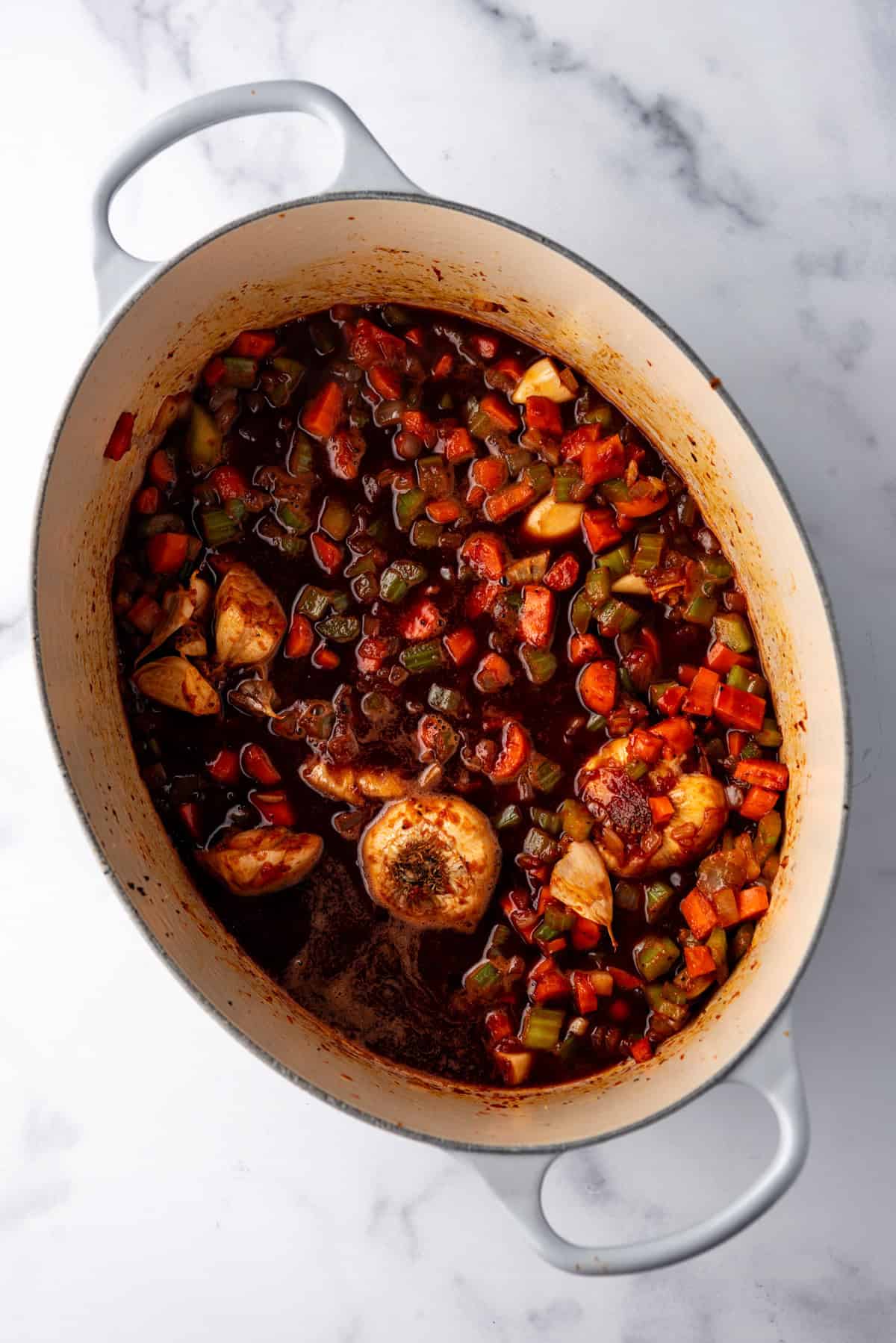 Overhead image of large dutch oven containing vegetables and sauce.