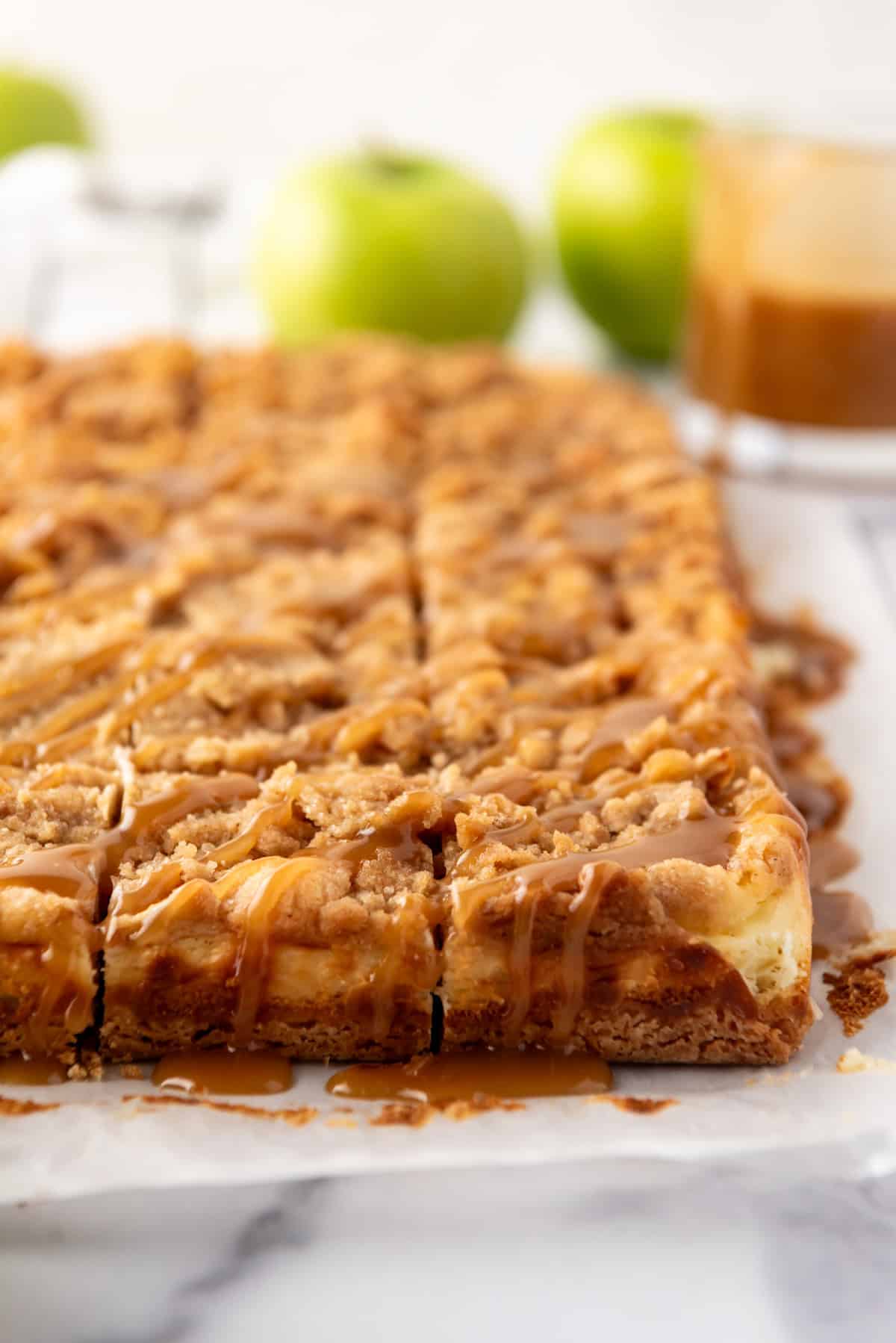 A side view of apple cheesecake bars drizzled with caramel sauce.