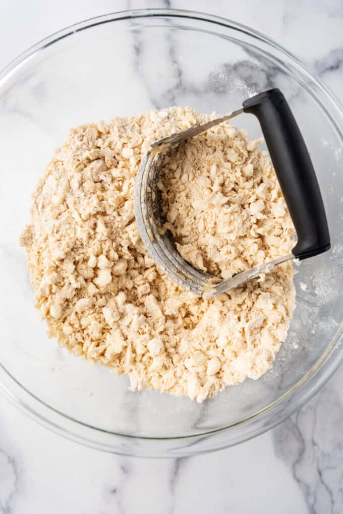 Overhead view of a pastry cutter in a glass bowl with the a sugar-flour-butter mixture resembling coarse crumbs.