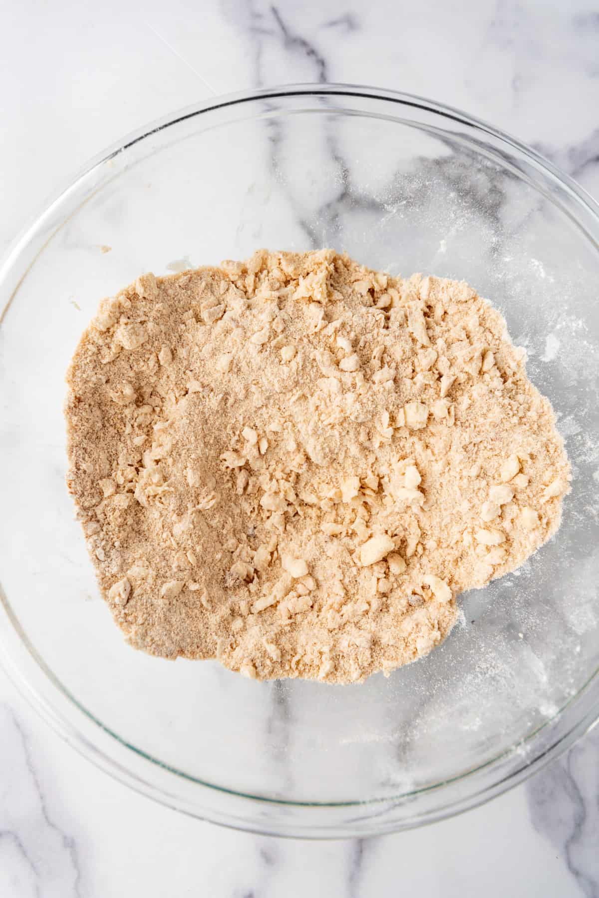 Overhead view of flour, brown sugar, oats, and cinnamon combined in a medium bowl.