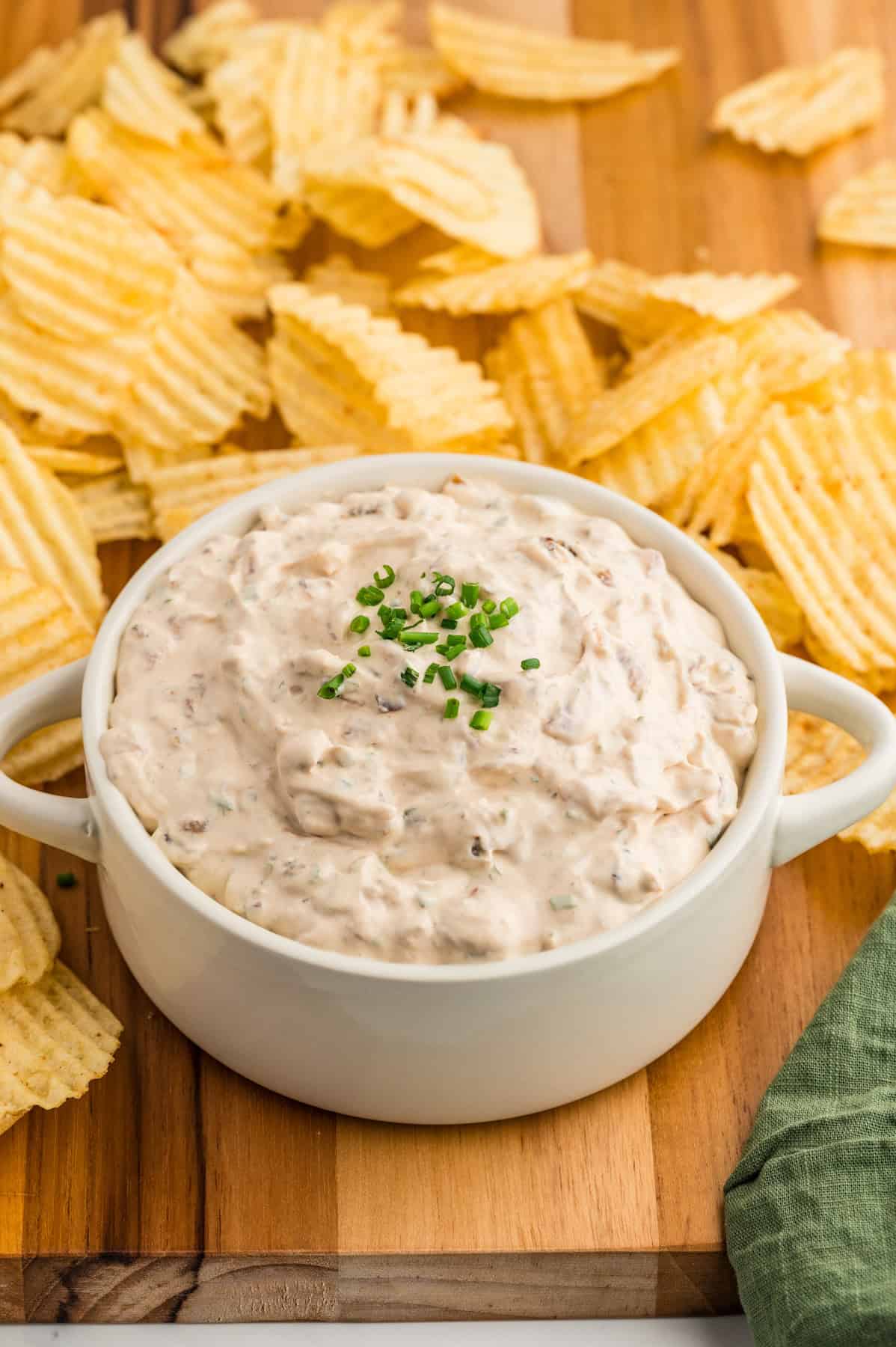 A bowl of homemade french onion dip next to ruffled potato chips.