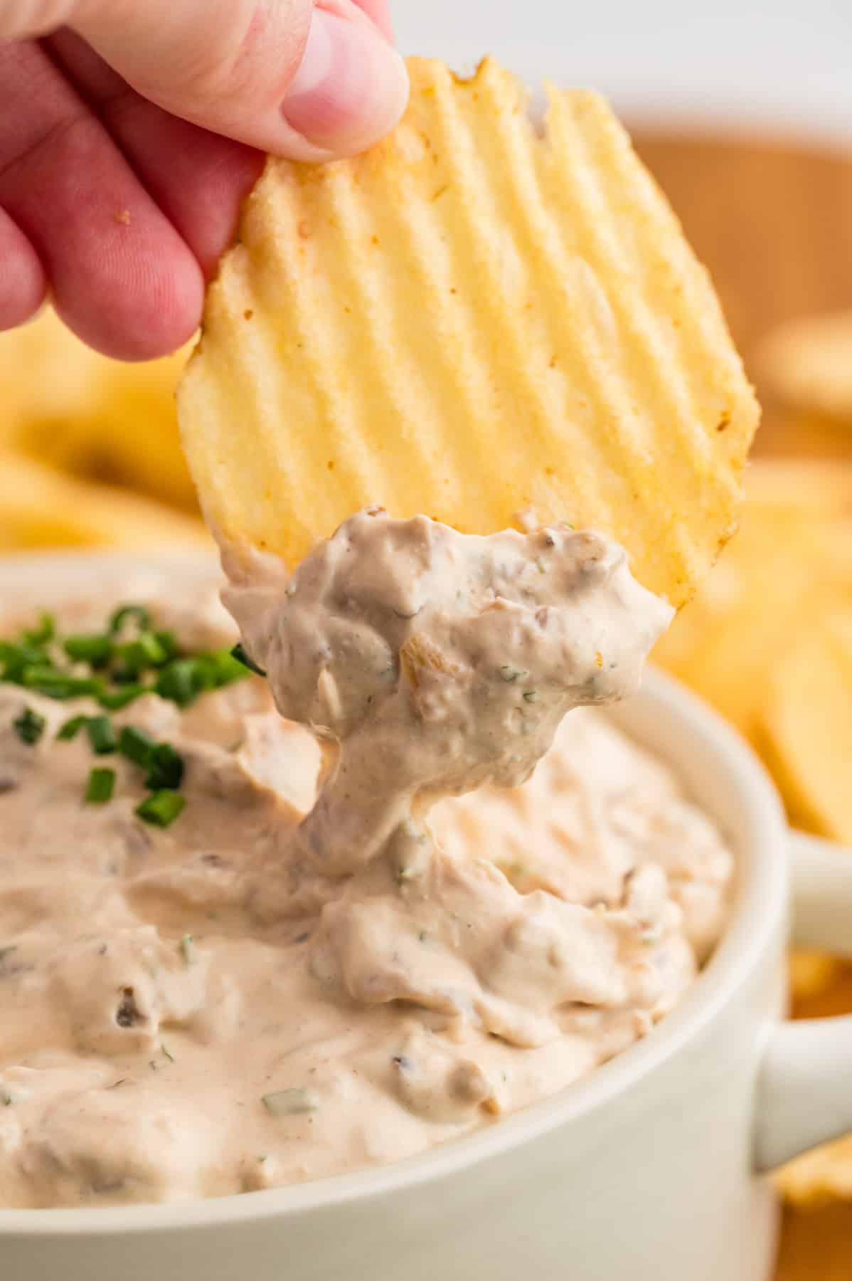 A hand holding a ruffled potato chip that has been dipped into a french onion dip.