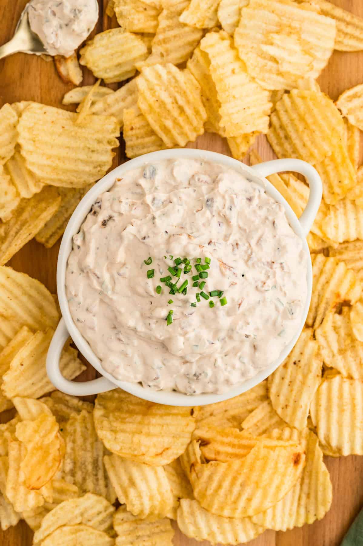 An overhead image of a bowl of french onion dip surrounded by ruffled potato chips.