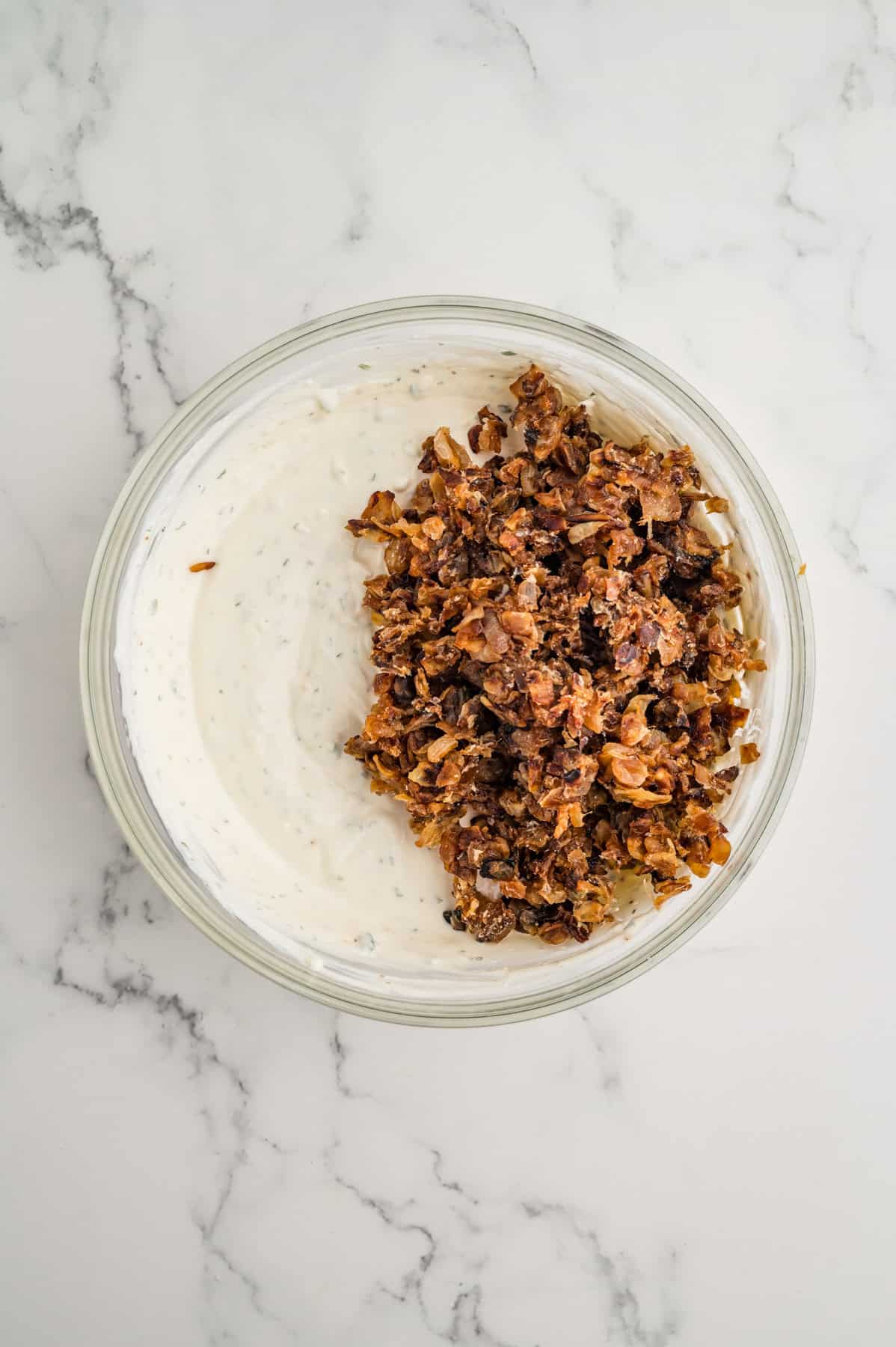 Adding caramelized onions to a homemade French onion dip in a glass mixing bowl.