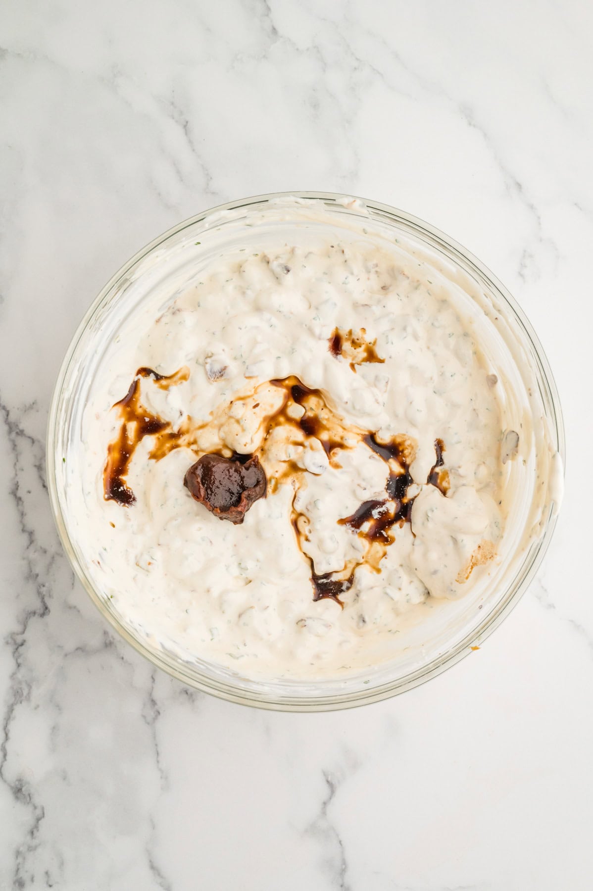 Addding worcestershire sauce and beef bouillon to a creamy french onion dip in a mixing bowl.