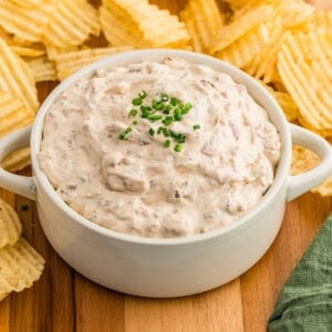 A bowl of homemade french onion dip next to ruffled potato chips.