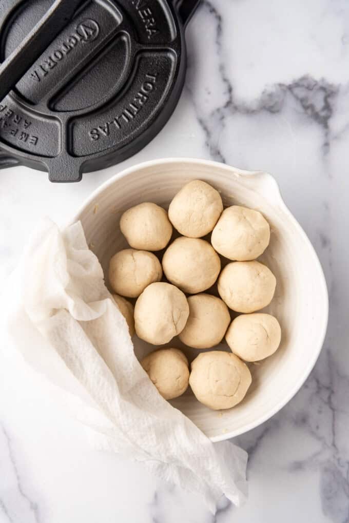 A bowl of balls of corn tortilla dough covered with a damp paper towel.