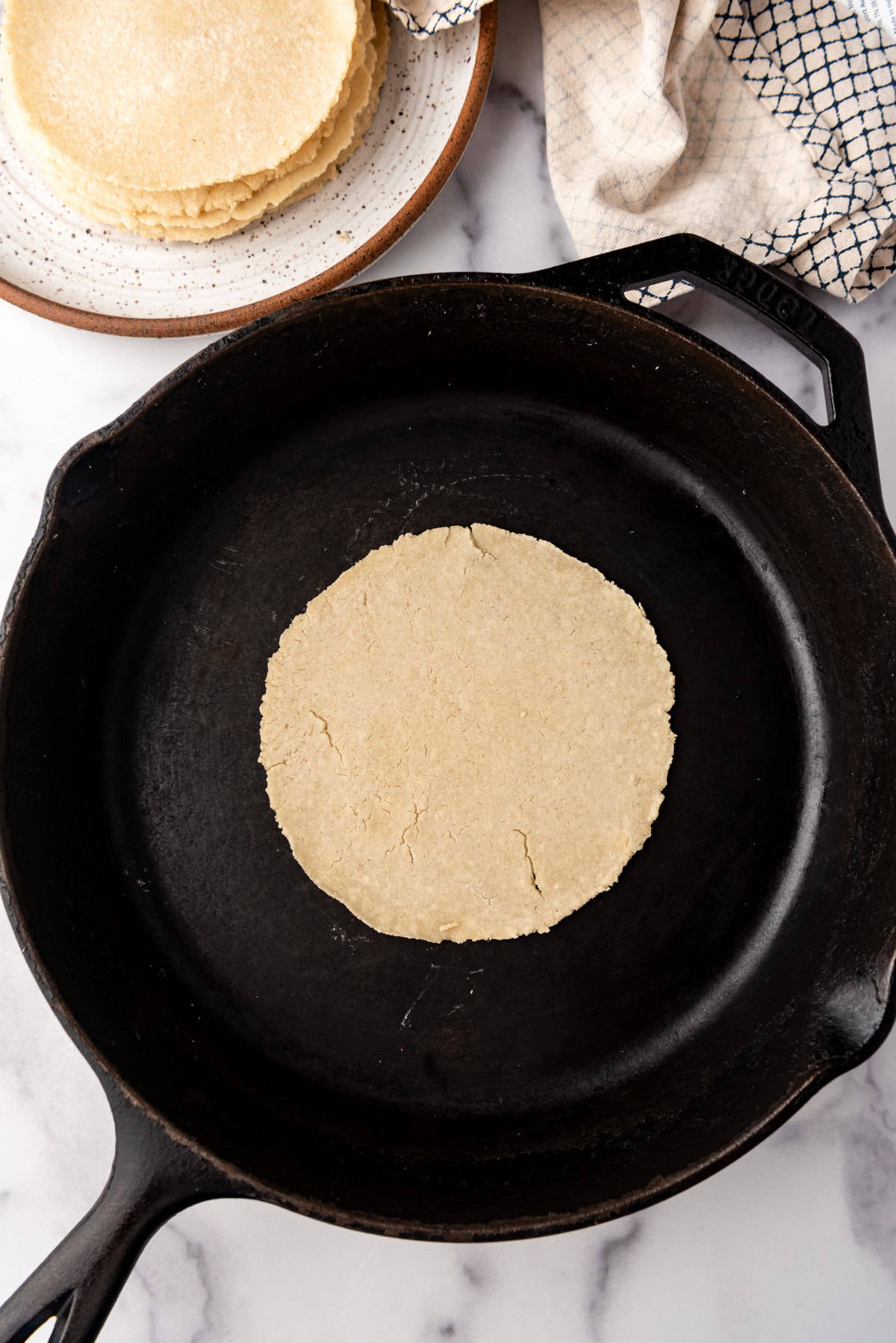 An overhead image of a corn tortilla being cooked in a cast iron skillet.