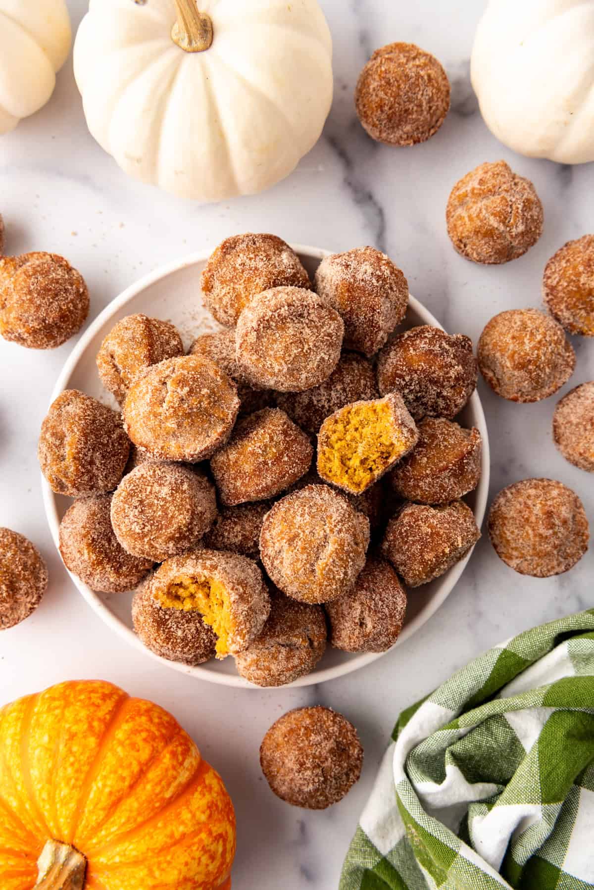 An overhead image of a plate of mini pumpkin donut muffins surrounded by small orange and white pumpkins.