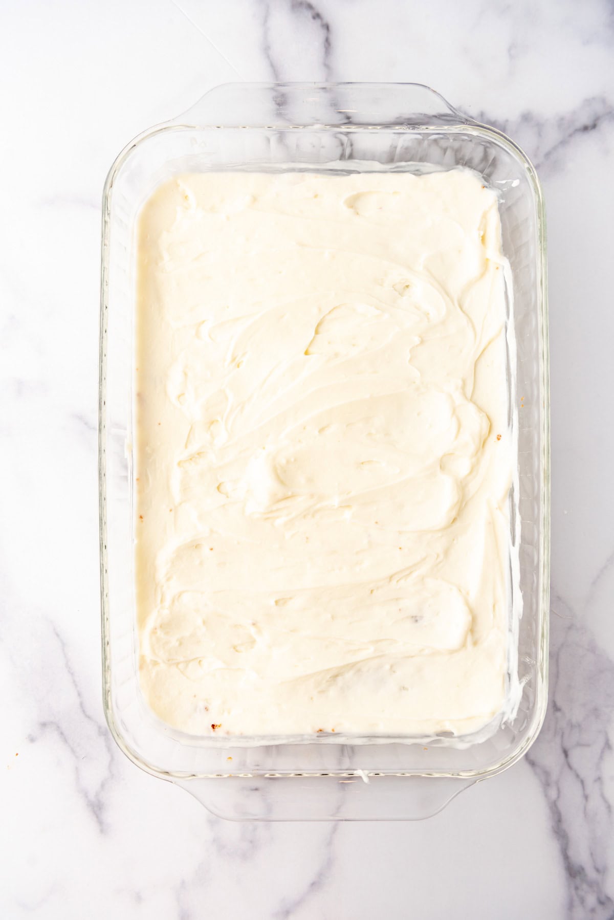 Spreading a layer of cream cheese filling in a 9x13-inch glass baking pan.