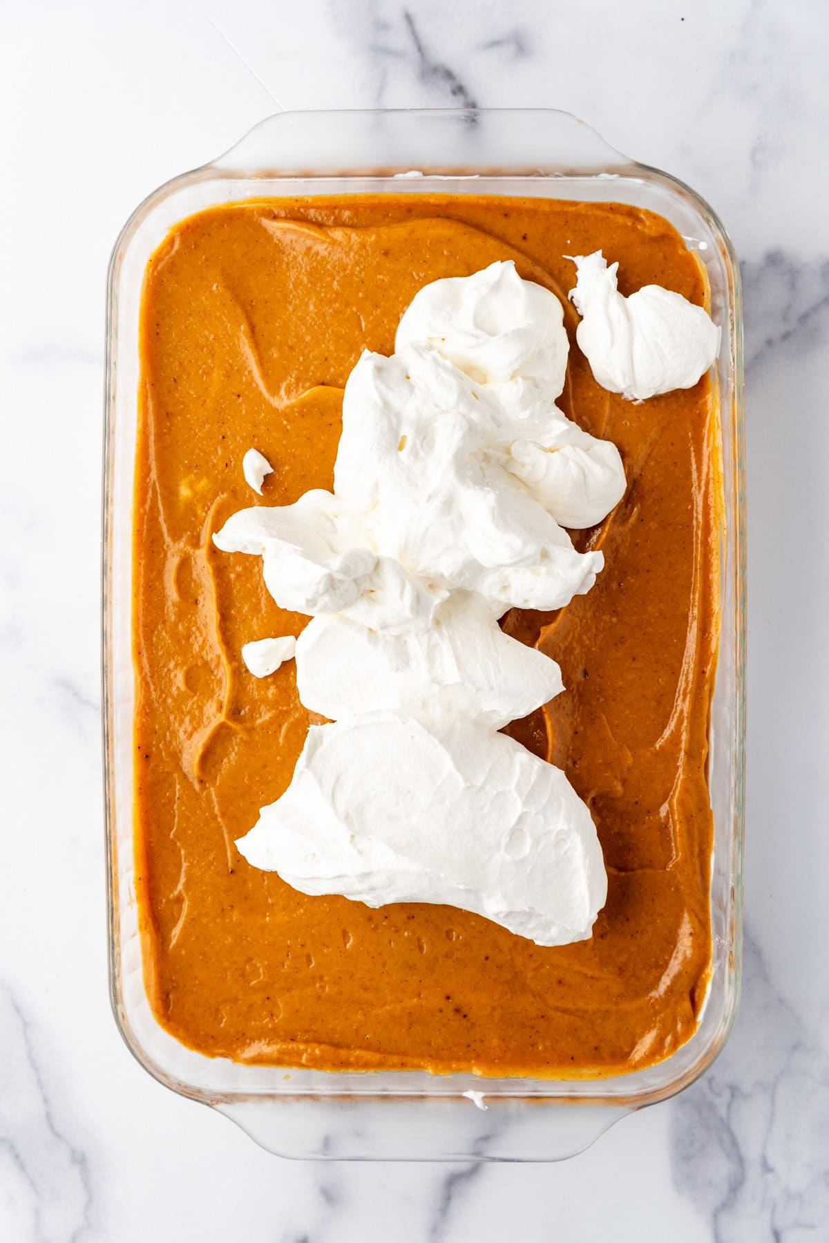 Adding a layer of whipped cream on top of a no-bake pumpkin delight dessert.