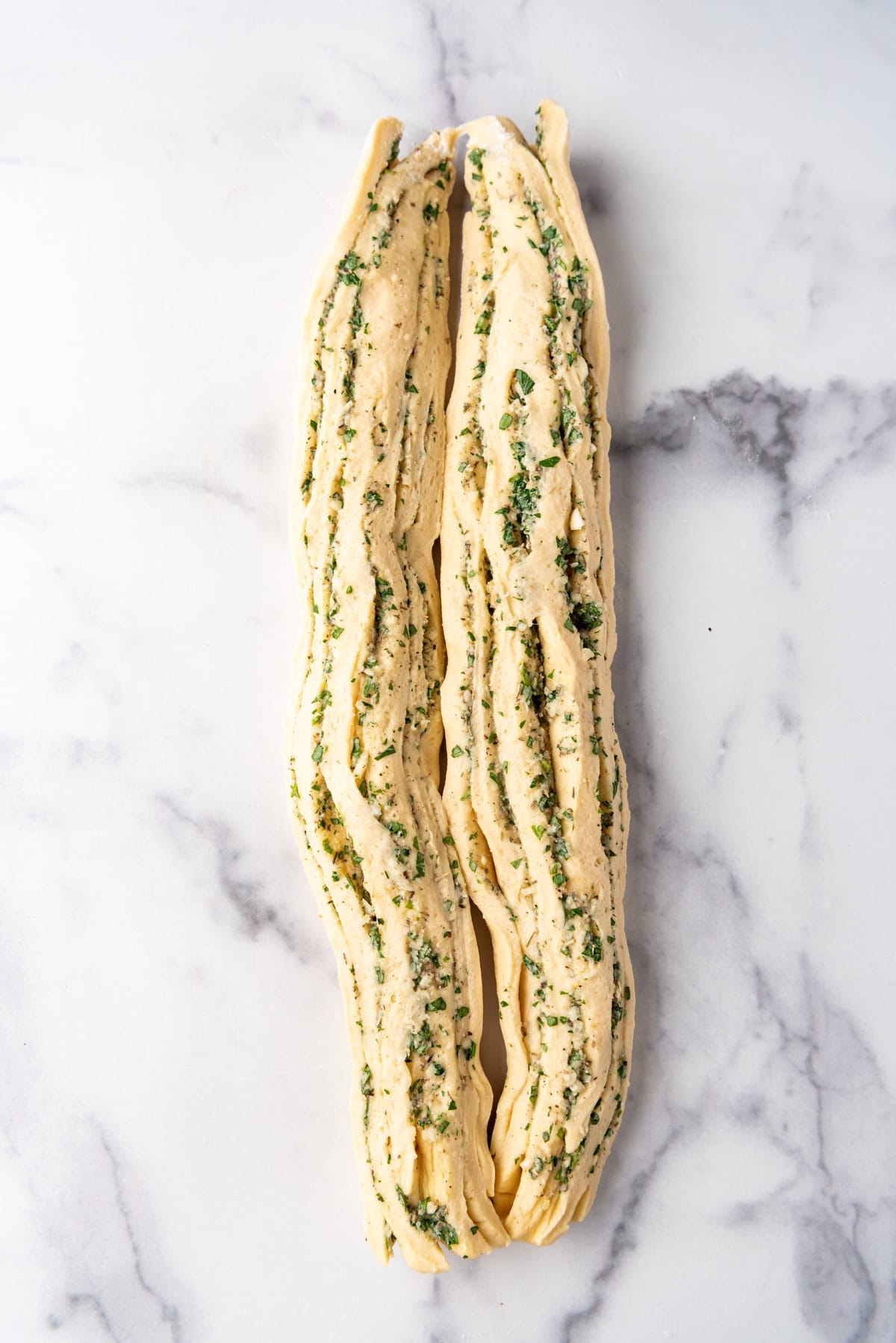 A rolled up loaf of garlic herb bread dough sliced in half.