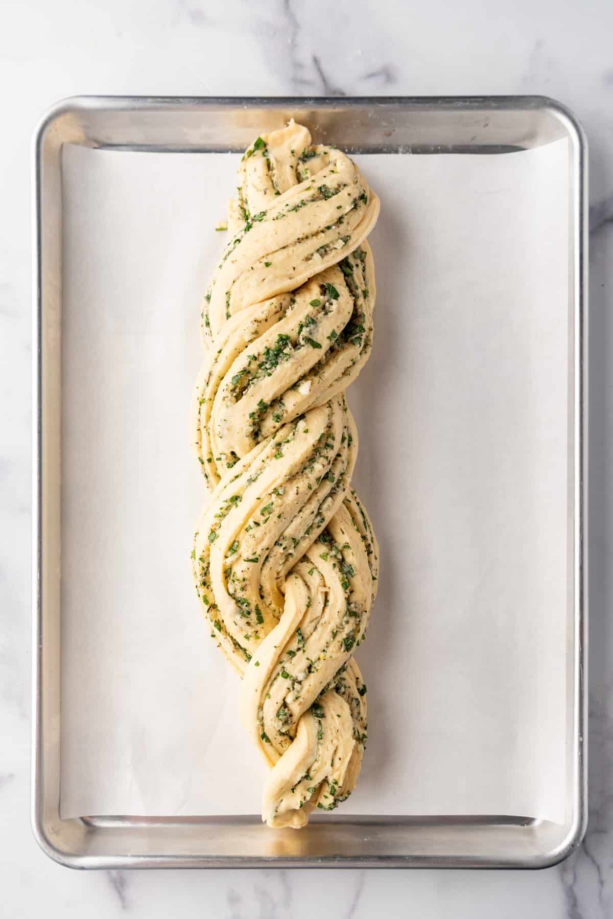 A twisted loaf of bread dough on a baking sheet lined with parchment paper.