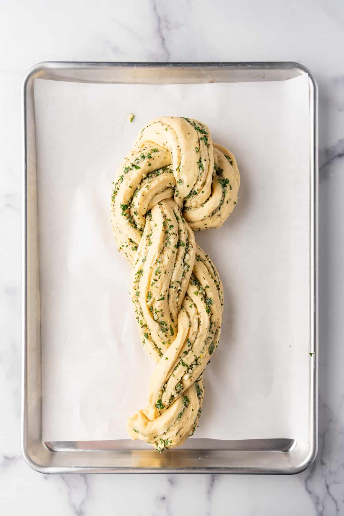 Twisting a braided loaf of garlic herb bread into an "S" shape.