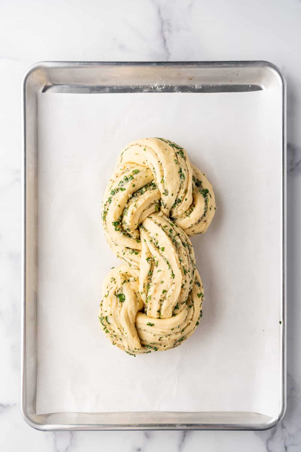 A shaped loaf of swirled garlic herb bread on a baking sheet.