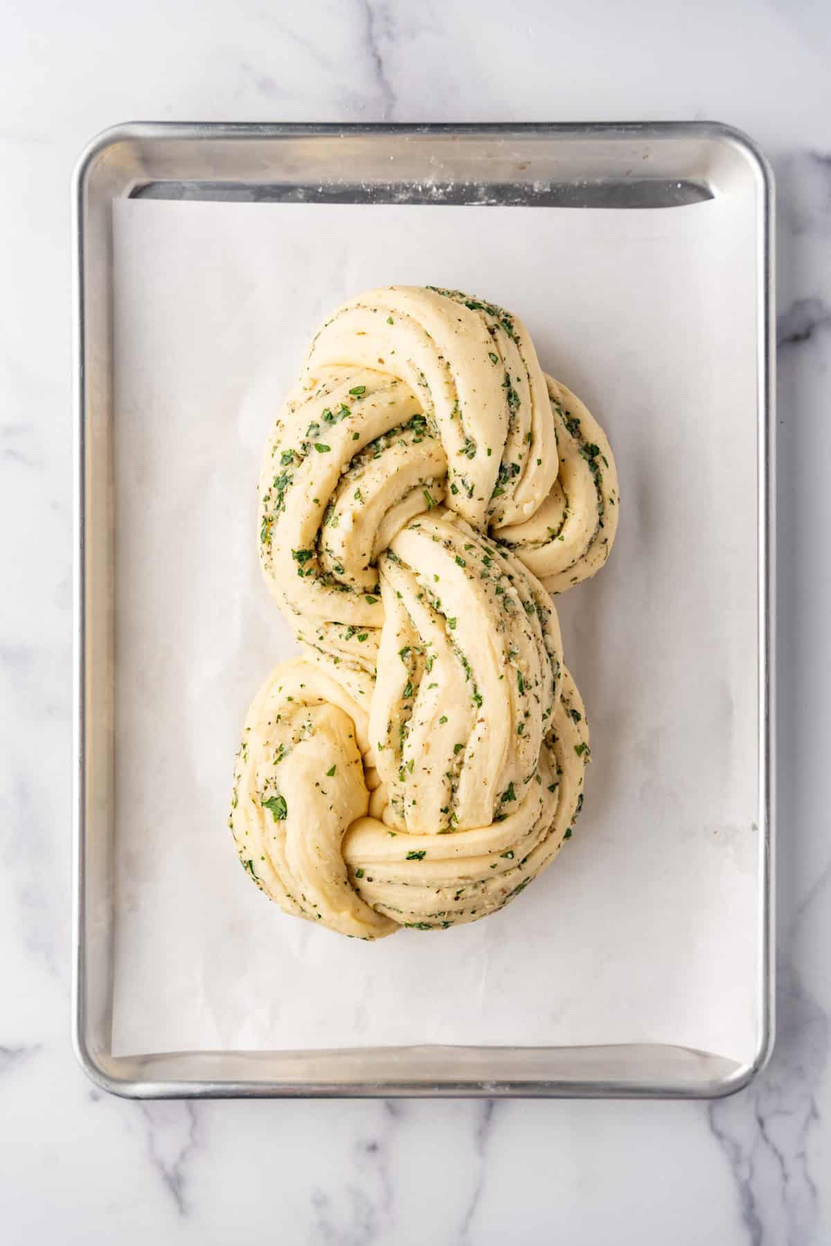 A puffy risen loaf of braided garlic herb bread on a baking sheet.