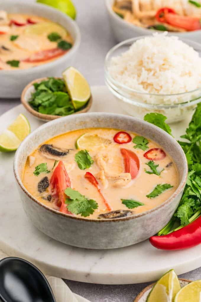 A side angle of a bowl of tom kha gai soup next to a bowl of rice.