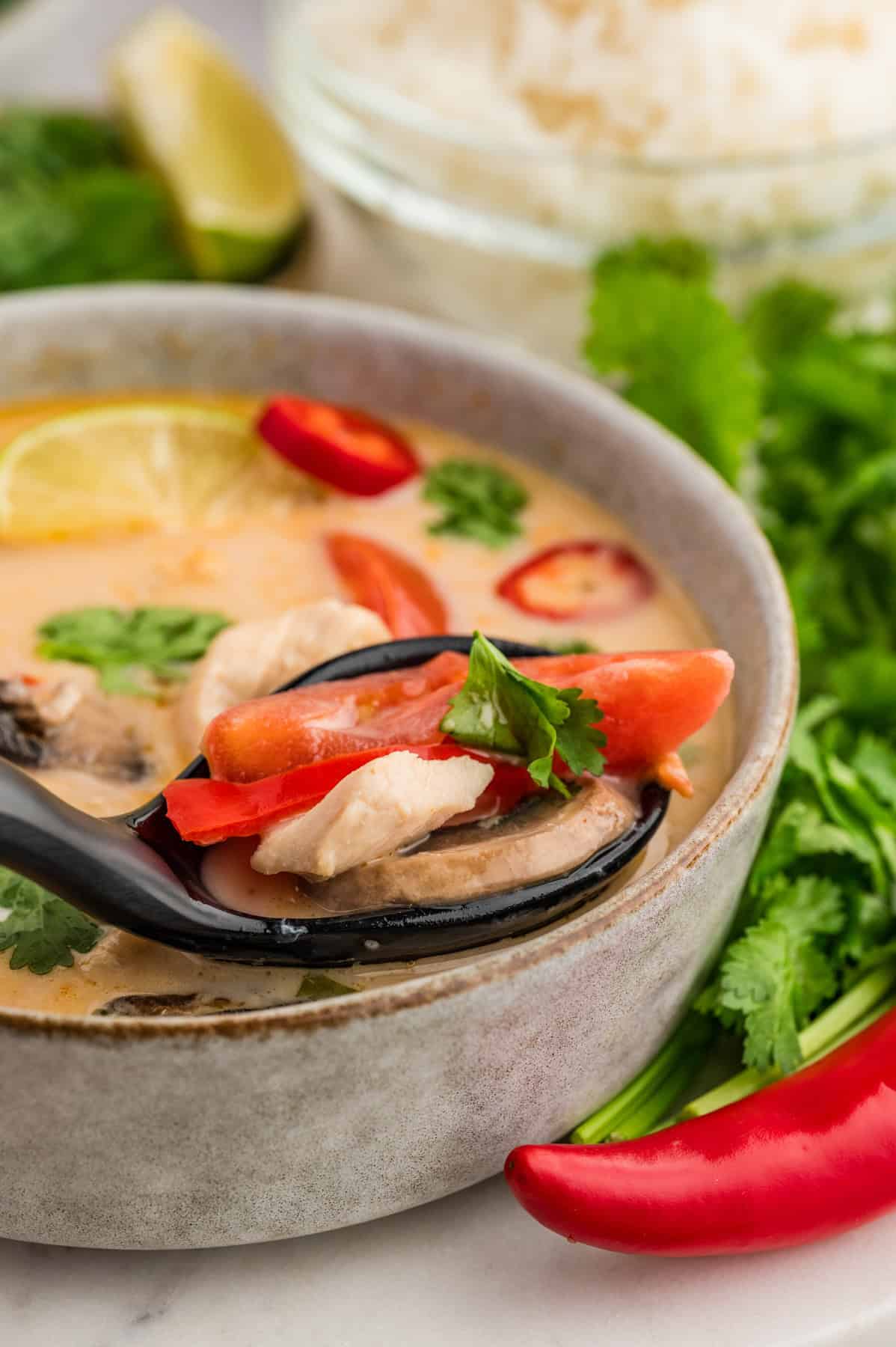 A spoonful of tom kha gai soup being lifted out of the bowl.