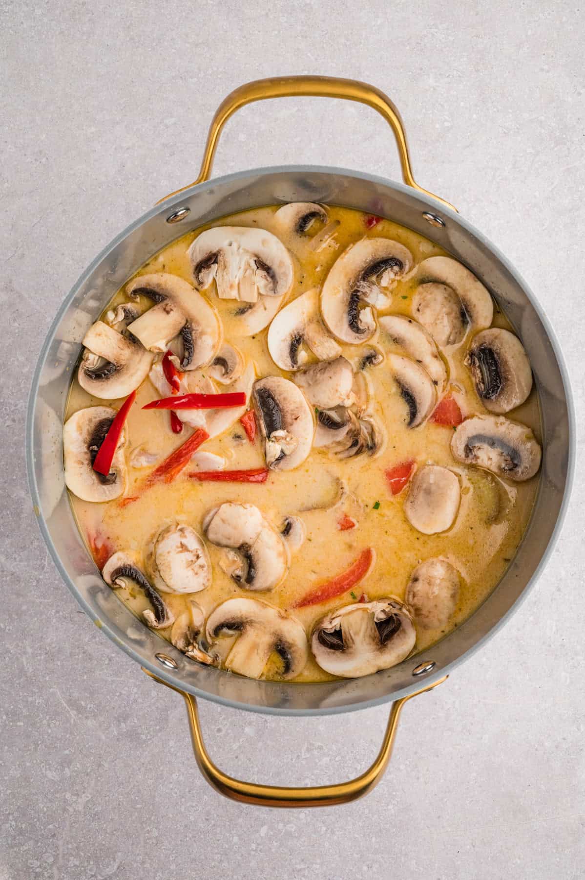 Adding mushrooms, peppers, and other ingredients to make tom kha gai soup.