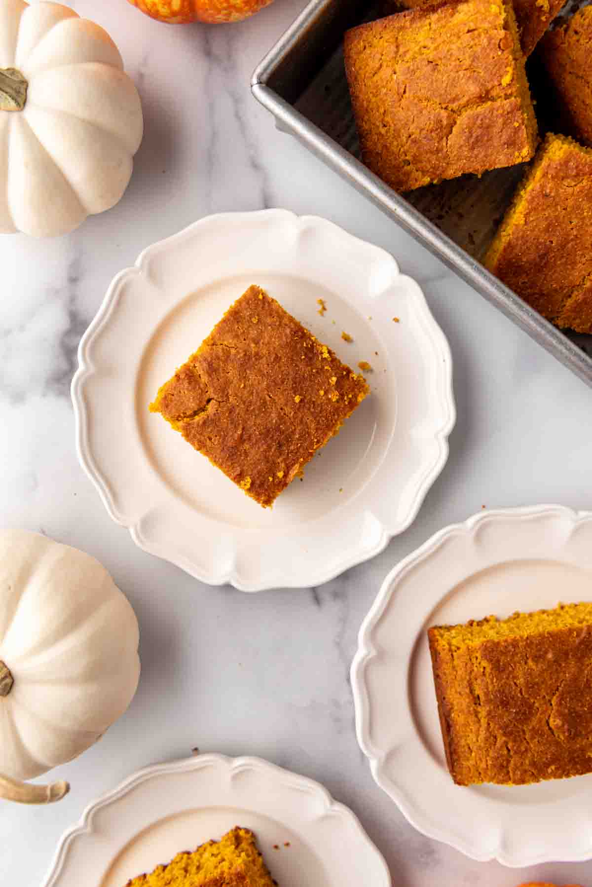 A close overhead image of a slice of pumpkin cornbread on a plate next to white pumpkins.